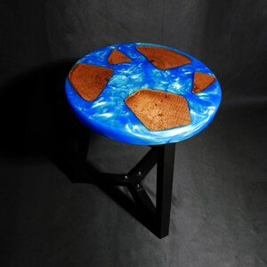 May include: A round side table with a blue resin top, featuring embedded wooden pieces. The table has a black metal base. The top's diameter is approximately 18 inches.