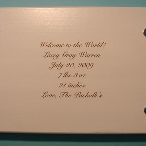 May include: A white wooden plaque with four silver metal feet. The plaque has a message engraved in brown ink that reads: "Welcome to the World! Lacey Gray Warren July 20, 2009 7 lbs 3 oz 21 inches Love, The Pasholk's"