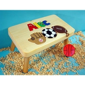 May include: Wooden step stool with a personalized name "Alex" in colorful letters and a sports theme. The top features a baseball glove, soccer ball, football, and basketball.