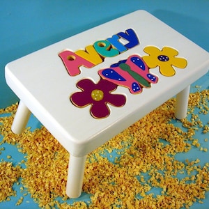 May include: White wooden step stool with a personalized name "Avery" spelled out in colorful puzzle pieces. The stool also features a butterfly and flower design.