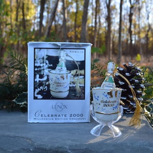 May include: A white Lenox Celebrate 2000 Millennium Edition ornament features a champagne bottle in a bucket. The ornament is packaged in a white box with the Lenox logo and the words "Celebrate 2000 Millennium Edition Ornament".
