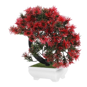 May include: A small, artificial bonsai tree with vibrant red and green foliage. The tree sits in a white, square-shaped pot with a curved black trunk. The pot has a small, grassy base.