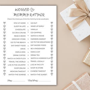 May include: A black and white game card titled "Would Mommy Rather" with a list of choices for a baby shower game. The card is on a beige surface with gift boxes in the background.