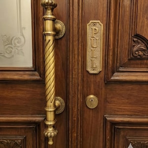 Könnte beinhalten: Nahaufnahme einer Holztür mit Messinggriff und "PULL"-Schild. Der Griff hat ein gedrehtes Design und die Tür hat ein Schlüsselloch. Die Tür ist aus dunkelbraunem Holz.
