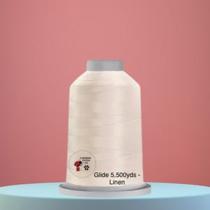 May include: A spool of off-white linen thread, labeled "Glide 5,500 yds - Linen," sits on a light blue platform against a pink backdrop. The thread spool has a gray top and a small logo with a mushroom and paw print.