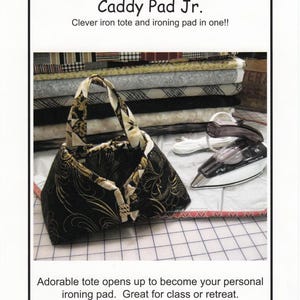 May include: A black fabric tote with gold swirl patterns that unfolds into an ironing pad. The text reads Sisters' Common Thread, Caddy Pad Jr., Clever iron tote and ironing pad in one!!, Adorable tote opens up to become your personal ironing pad. Great for class or retreat. With Heat-Resistant Lining included, Sized to hold your 6"-8 1/4" travel iron.