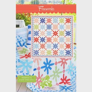 May include: A colorful quilt with a starburst pattern in shades of red, blue, pink, and green. The quilt is displayed on a bed with matching pillows and a patterned blanket. The text "Fireworks" is at the top.