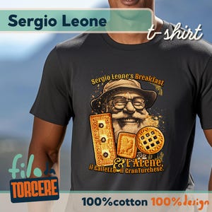 May include: A dark grey t-shirt with the text "Sergio Leone" at the top and "t-shirt" on the right. The shirt features a graphic of a smiling man with a hat and glasses, surrounded by cookies. The text "Sergio Leone's Breakfast" is above the graphic.