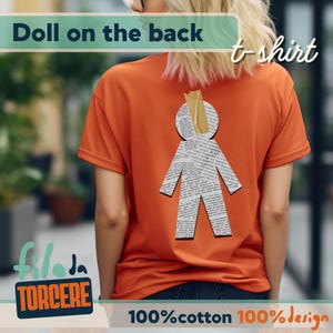 Puede incluir: Camiseta naranja con un diseño de muñeca de papel en la espalda. La muñeca está hecha de papel de periódico y tiene un trozo de cinta adhesiva en la cabeza. La camiseta tiene el texto "Doll on the back" y "t-shirt". La parte inferior de la camiseta dice "100% cotton 100% design".