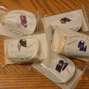 May include: Five small white bags with goat milk soap bars inside. Each bag has a label with a goat image, a bible verse, and a scent name. The scents are Moonlight, Coconut Lime Verbena, Lemongrass Essential, Crooke, and Adara.