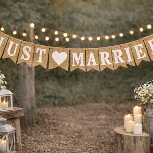 May include: A rustic wedding scene with a burlap banner that reads "JUST MARRIED" in white letters and a white heart. The scene includes lanterns, flowers, candles, and string lights, creating a romantic ambiance.