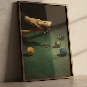 Puede incluir: Impresi&oacute;n enmarcada de una escena de naturaleza muerta con una copa de martini y bolas de billar sobre una mesa de fieltro verde. La obra de arte tiene una est&eacute;tica vintage, con una mano sosteniendo el c&oacute;ctel. Las bolas son de varios colores, incluyendo naranja, verde y azul.