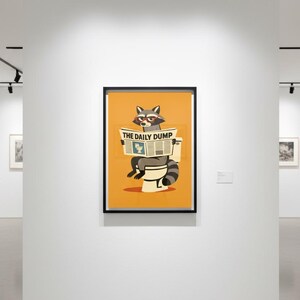 Op de afbeelding: Ingelijste kunstprint met een wasbeer met een bril die de krant "THE DAILY DUMP" leest op een toilet. Het kunstwerk heeft een oranje achtergrond en wordt in een galerij tentoongesteld.