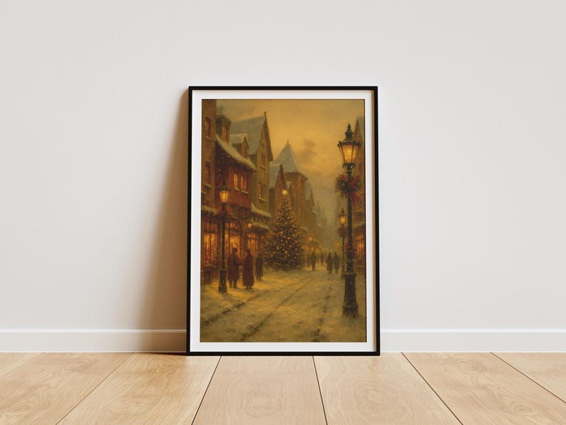 May include: Framed print of a winter street scene. Snow-covered buildings line a cobblestone street, illuminated by streetlights and shop windows. A Christmas tree stands in the distance, with figures walking along the street.