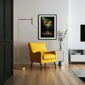 Puede incluir: Un cuadro con una imagen de una copa de martini cuelga sobre un sill&oacute;n amarillo. Una l&aacute;mpara de pie dorada y una peque&ntilde;a mesa auxiliar con un jarr&oacute;n de flores tambi&eacute;n est&aacute;n en la habitaci&oacute;n. La habitaci&oacute;n tiene pisos de madera y una pared blanca.