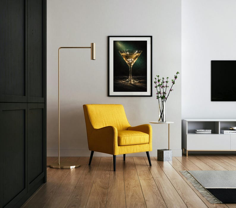 Puede incluir: Un cuadro con una imagen de una copa de martini cuelga sobre un sill&oacute;n amarillo. Una l&aacute;mpara de pie dorada y una peque&ntilde;a mesa auxiliar con un jarr&oacute;n de flores tambi&eacute;n est&aacute;n en la habitaci&oacute;n. La habitaci&oacute;n tiene pisos de madera y una pared blanca.