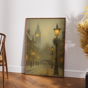 Pu&ograve; includere: Una stampa incorniciata di una scena di strada vintage in una tavolozza di colori tenui. L'opera raffigura una strada nebbiosa con lampioni, edifici e una torre dell'orologio sullo sfondo. Il tema generale &egrave; un paesaggio urbano storico.