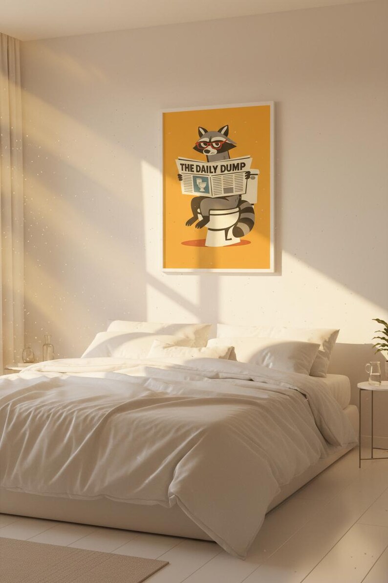 Op de afbeelding: Een ingelijste poster met een gele achtergrond met een wasbeer die een krant met de titel "THE DAILY DUMP" leest op een toilet. De poster hangt boven een bed met wit beddengoed.