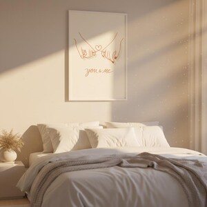 Puede incluir: Una habitaci&oacute;n con una cama con ropa de cama blanca y una manta gris. Una impresi&oacute;n enmarcada en la pared muestra un dibujo lineal de dos manos tomadas del dedo me&ntilde;ique, con las palabras "you & me". Un jarr&oacute;n con plantas secas est&aacute; en la mesita de noche.
