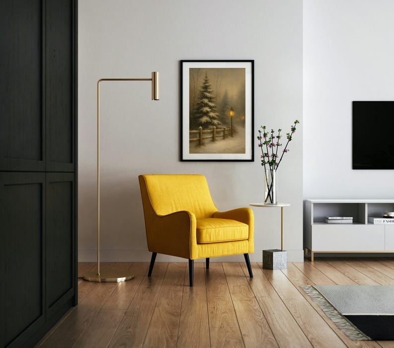 May include: A cozy living room scene featuring a framed winter landscape painting, a bright yellow armchair, and a gold floor lamp. The room has hardwood floors and a modern white cabinet. A vase of flowers sits on a small side table.