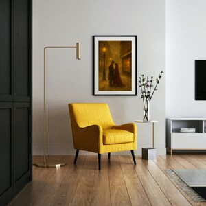 May include: A framed print shows a couple in a romantic embrace on a cobbled street, lit by streetlights. The artwork is in a black frame, above a yellow armchair. The room has a modern design with a wooden floor.