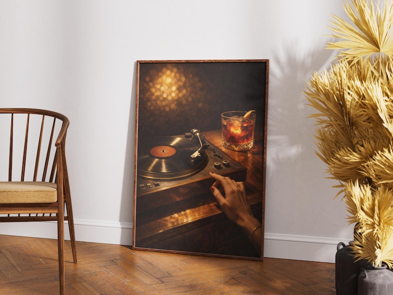May include: A framed print depicting a vintage record player with a vinyl record and a cocktail. The image has a warm colour palette, with a hand reaching towards the record player. The print is in a wooden frame.