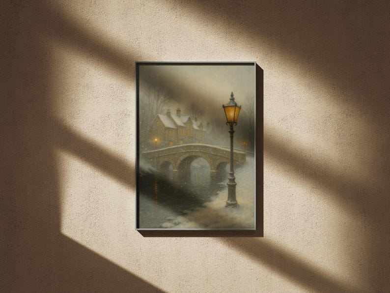 May include: Framed art print depicting a snowy winter scene. A stone bridge arches over a river, leading to snow-covered buildings. A lit lamppost stands in the foreground, casting a warm glow in the cold, misty atmosphere.