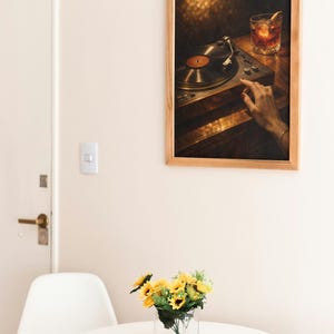 May include: A framed print showing a vintage record player and a cocktail glass. The artwork is set against a warm, blurred background. A small vase of sunflowers sits on a white table. The room has a minimalist design.