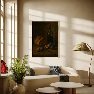 Pode incluir: Uma pintura emoldurada de natureza morta retrata p&atilde;o, figos, uma faca e uma garrafa de vinho. A pintura est&aacute; sobre um fundo escuro. A sala apresenta um sof&aacute; creme, duas mesas de centro redondas e uma lumin&aacute;ria de ch&atilde;o com uma tela verde.