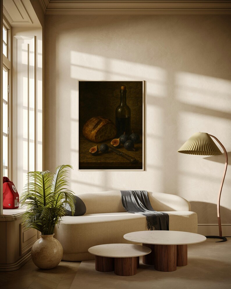 Pode incluir: Uma pintura emoldurada de natureza morta retrata p&atilde;o, figos, uma faca e uma garrafa de vinho. A pintura est&aacute; sobre um fundo escuro. A sala apresenta um sof&aacute; creme, duas mesas de centro redondas e uma lumin&aacute;ria de ch&atilde;o com uma tela verde.