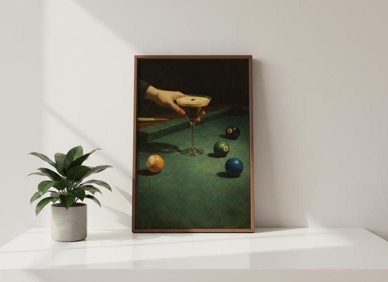 Puede incluir: Una impresi&oacute;n enmarcada representa un c&oacute;ctel sobre una mesa de billar con bolas. Una mano sostiene la copa de martini con una bebida oscura y espuma. La mesa de billar es verde y las bolas son amarillas, verdes, negras y azules.