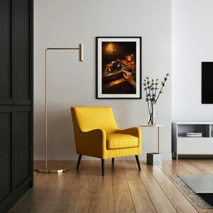 May include: A contemporary living room featuring a yellow armchair, a gold floor lamp, and a framed picture of a record player. The room has wooden flooring and a white side table with a vase of flowers.