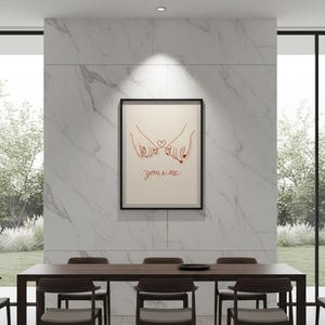Puede incluir: Un cuadro enmarcado con un dibujo lineal de dos manos con los me&ntilde;iques entrelazados y un coraz&oacute;n. Las palabras "you & me" est&aacute;n escritas en rojo. El cuadro cuelga sobre una mesa de comedor de madera oscura con sillas a juego.
