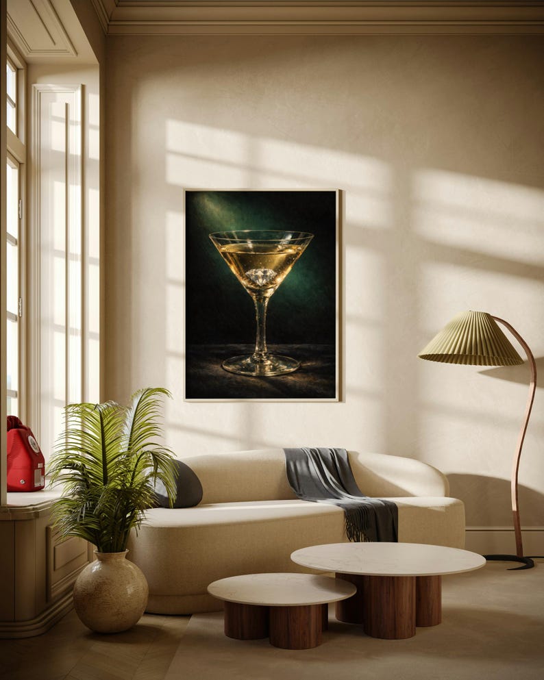 Puede incluir: Una impresi&oacute;n enmarcada de un c&oacute;ctel en una copa de martini. La bebida es dorada, con un cubito de hielo transparente. La impresi&oacute;n cuelga sobre un sof&aacute; color crema con una manta gris. Dos mesas de centro redondas con bases de madera est&aacute;n frente al sof&aacute;.