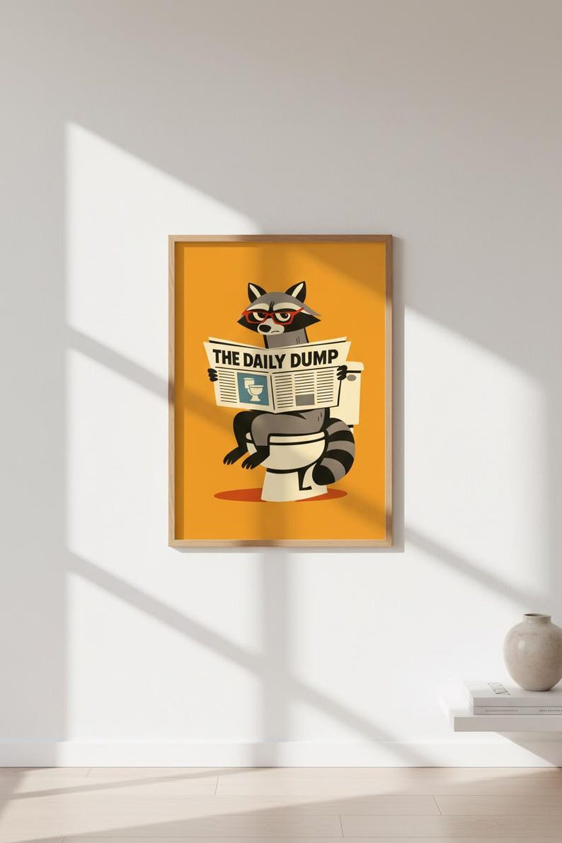 Op de afbeelding: Een ingelijste print met een wasbeer met een bril die een krant leest met de titel "THE DAILY DUMP" terwijl hij op een toilet zit. Het kunstwerk heeft een gele achtergrond en een humoristisch thema.