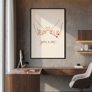 Puede incluir: Un cuadro enmarcado con un dibujo lineal minimalista en rojo de dos manos entrelazadas por los me&ntilde;iques, con un coraz&oacute;n y las palabras "you & me". La obra de arte se exhibe en un entorno de oficina moderno.