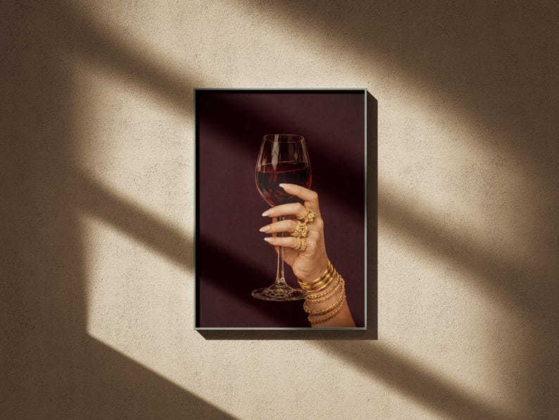 Peut inclure: Impression d'art encadr&eacute;e d'une main tenant un verre de vin rouge. La main est orn&eacute;e de bracelets et de bagues dor&eacute;es. Le fond est bordeaux fonc&eacute;, cr&eacute;ant une ambiance &eacute;l&eacute;gante.