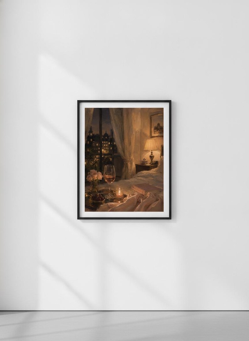 May include: A framed wall art print depicting a cozy bedroom scene at night. The image features a bed with rumpled white linens, a glass of wine, a small vase of flowers, and a glowing lamp on a nightstand, with a city view through a window.