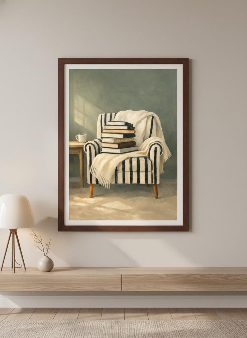 K&ouml;nnte beinhalten: Ein gerahmter Druck eines gem&uuml;tlichen Leseecks. Das Bild zeigt einen gestreiften Sessel mit einem Stapel B&uuml;cher und einer wei&szlig;en Decke. Ein kleiner Tisch mit einer Kaffeetasse steht daneben und schafft eine warme und einladende Atmosph&auml;re.