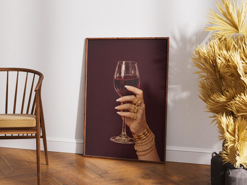 Peut inclure: Impression encadr&eacute;e d'une main tenant un verre de vin rouge. La main est orn&eacute;e de bagues et de bracelets dor&eacute;s. Le fond est bordeaux fonc&eacute; et le cadre est marron.