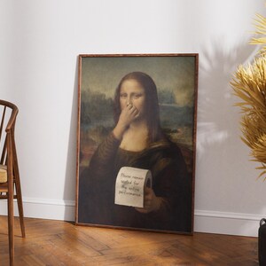 May include: A framed print of the Mona Lisa with a humorous twist. The iconic figure covers her nose with her hand and holds a roll of toilet paper with the text "Please remain seated for the entire performance."