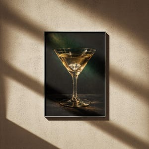 Puede incluir: Una impresi&oacute;n enmarcada que presenta una copa de martini llena de un l&iacute;quido dorado y un objeto en forma de diamante. El vaso est&aacute; centrado contra un fondo oscuro con acentos verdes y dorados. La impresi&oacute;n se muestra en una pared beige con sombras.