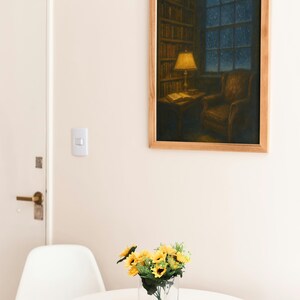 Peut inclure: Peinture encadr&eacute;e d'une sc&egrave;ne de biblioth&egrave;que avec une lampe allum&eacute;e, un fauteuil et une fen&ecirc;tre sur une nuit &eacute;toil&eacute;e. Une petite table avec un vase de tournesols est devant une table et une chaise blanches.