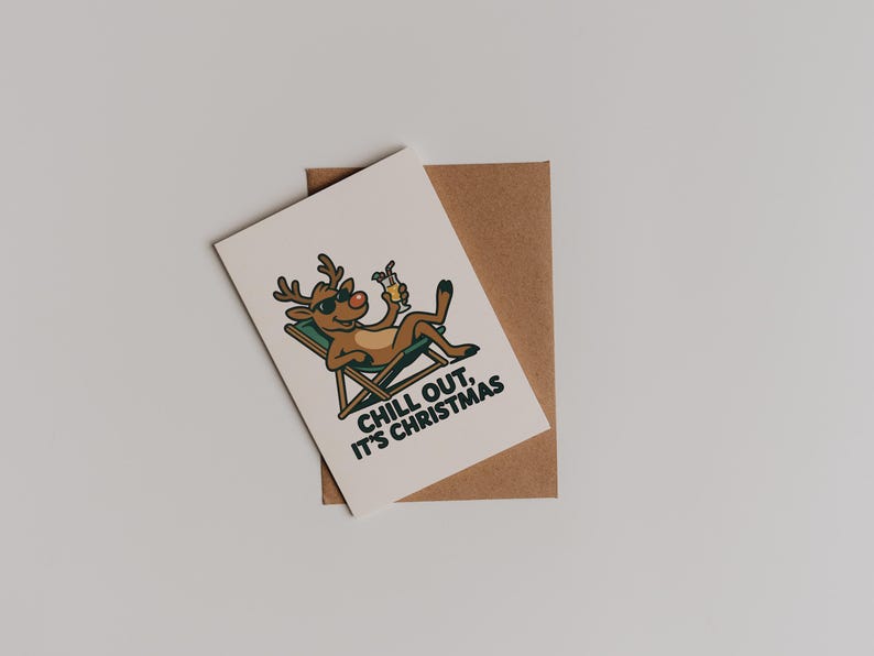 Pu&ograve; includere: Un biglietto di Natale con una renna dei cartoni animati con occhiali da sole, che si rilassa su una sedia a sdraio e tiene in mano un cocktail. Il biglietto riporta la scritta "CHILL OUT, IT'S CHRISTMAS" ed &egrave; posto su una busta marrone.
