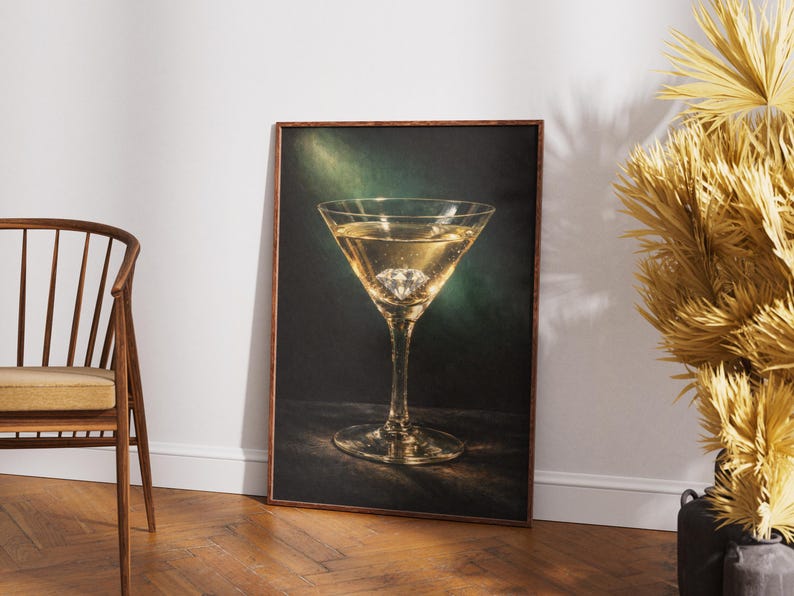 Puede incluir: Impresi&oacute;n enmarcada que presenta una copa de martini llena de un l&iacute;quido dorado y un diamante. El vaso est&aacute; centrado sobre un fondo oscuro con un efecto de luz verde y dorada. La impresi&oacute;n se exhibe sobre un suelo de madera junto a una silla de madera.
