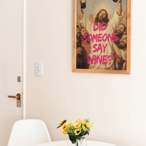 A framed funny altered art poster of Jesus holding two wine bottles with the neon pink text 'Did Someone Say Wine?', perfect for eclectic kitchen or home bar decor.
