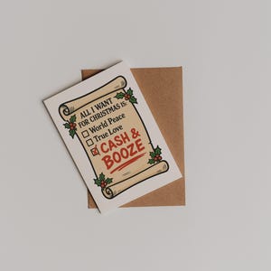 Puede incluir: Tarjeta de felicitaci&oacute;n navide&ntilde;a con dise&ntilde;o de pergamino, con el texto "All I want for Christmas is: World Peace, True Love, Cash & Booze." La tarjeta est&aacute; sobre un sobre marr&oacute;n, con acebo y bayas.