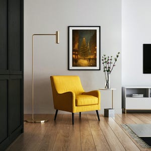May include: A framed art print depicts a Christmas tree in a snowy town square, lit with golden lights. A yellow armchair with black legs sits below the artwork. A gold floor lamp and a white side table with a vase of flowers complete the scene.