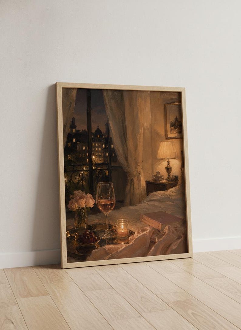 May include: A framed art print depicting a cozy bedroom interior at night. A bedside lamp illuminates a book, a glass of rose wine, a small vase of pink flowers, and a candle on a tray. A window reveals a dark city skyline with glowing lights.