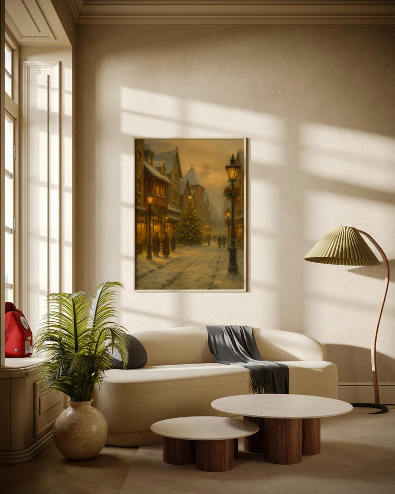 May include: A framed painting depicts a snowy street scene with buildings, a Christmas tree, and figures. The artwork hangs above a cream-colored sofa with a gray throw, two round coffee tables, a floor lamp, and a potted plant.